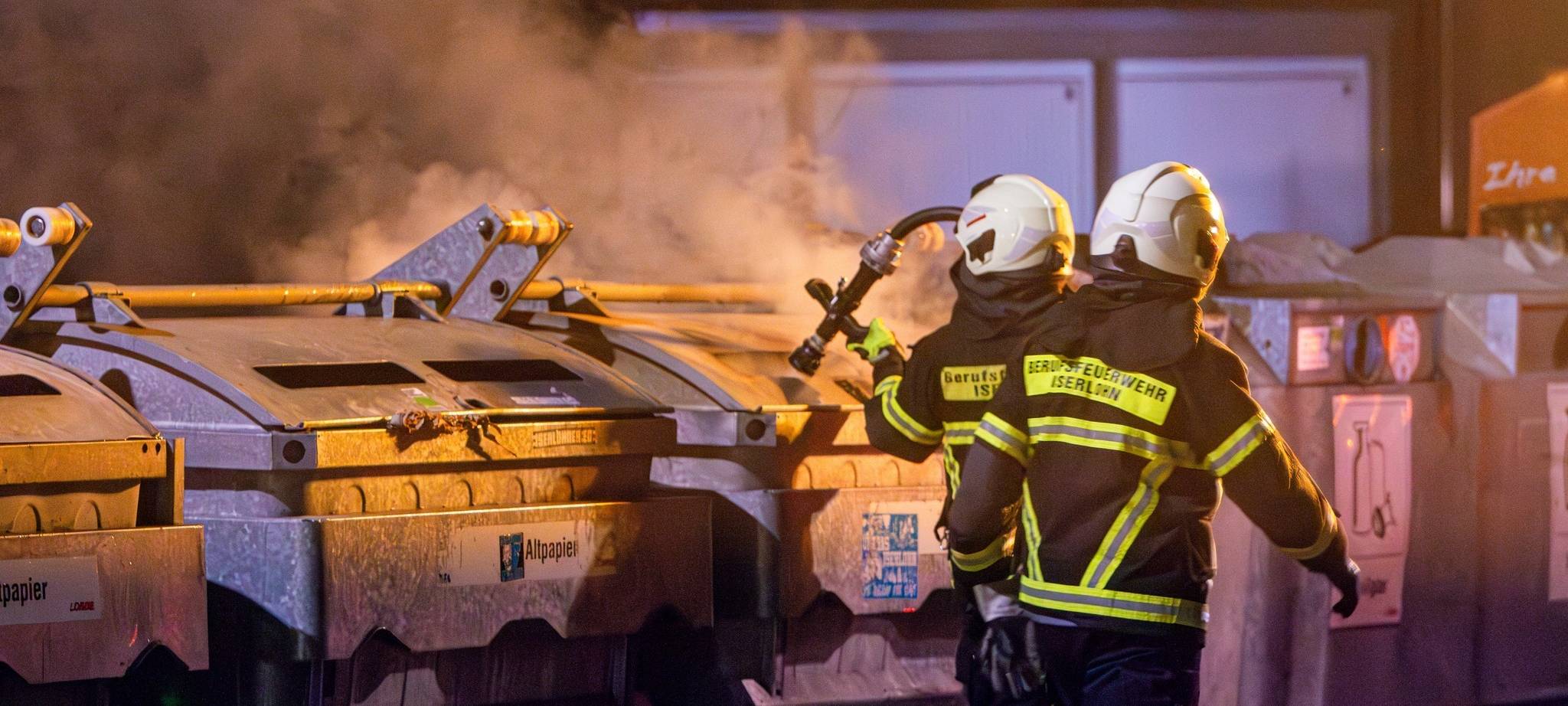 Einsatzkräfte der Feuerwehr löschen brennende Müll- und Papiercontainer.