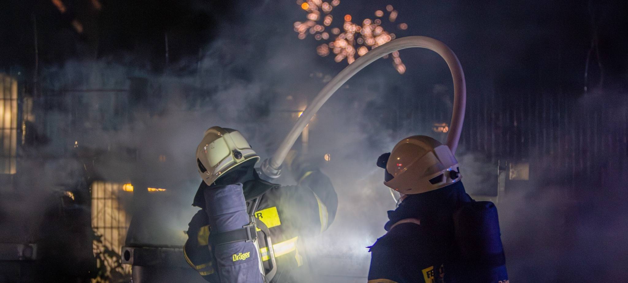Feuerwehrmänner löschen noch während des Feuerwerks einen Müllcontainer.